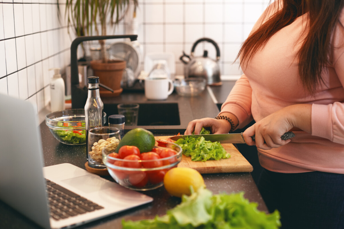 unrecognizable-plus-size-female-standing-at-kitchen-counter-and-cutting-fresh-organic-vegetables-on-chopping-board-making-healthy-low-calories-salad-while-watching-movie-online-on-laptop-computer Otyłość a zaburzenia odżywiania – perspektywa psychodietetyczna  